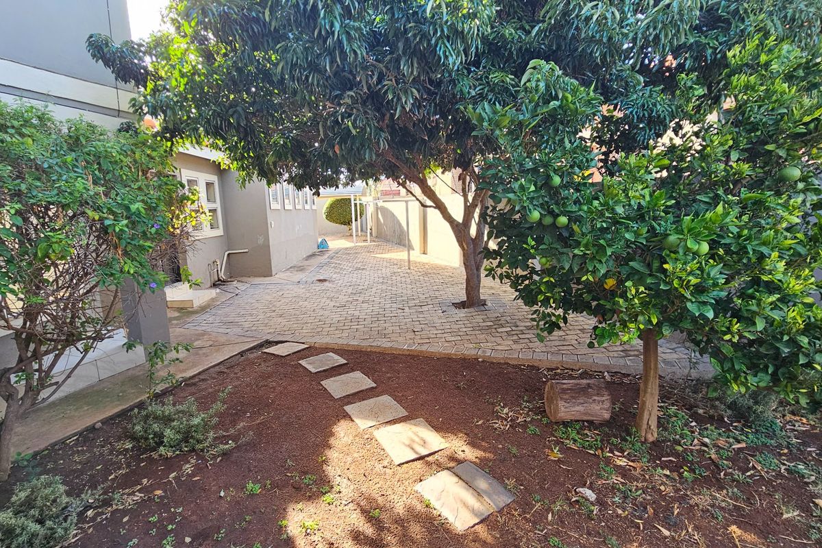 A private rear garden area featuring paved walkways, mature trees, and established landscaping adjacent to the building exterior.