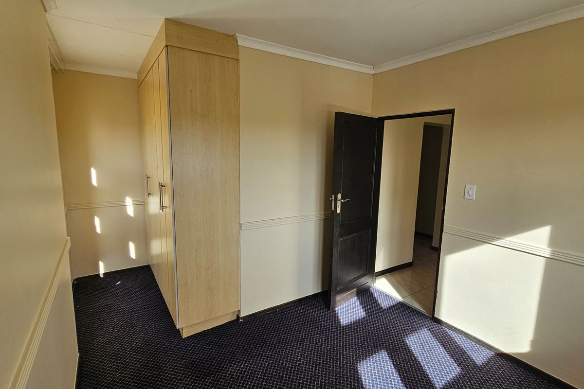 A bedroom featuring built-in wooden cupboards, dark carpeting, and a doorway leading to an adjacent hallway.