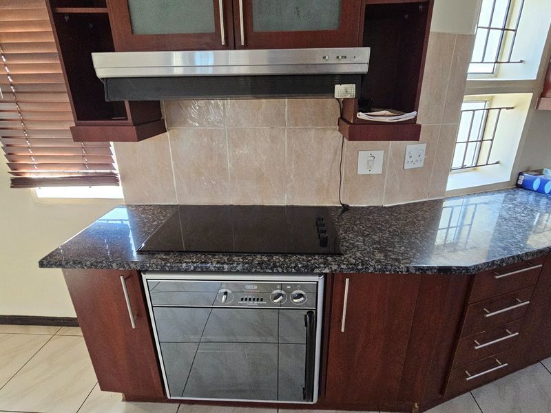 A functional kitchen area featuring dark wood cabinetry, granite countertops, a built-in oven, and a glass cooktop with an extractor fan.