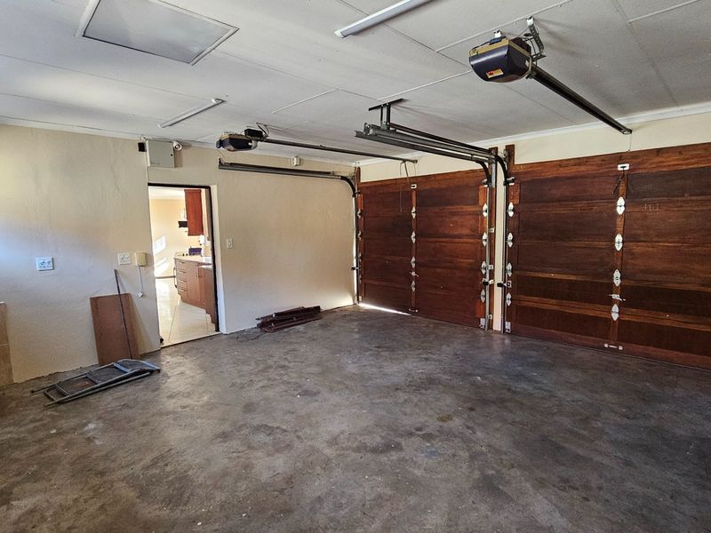 A spacious double garage featuring wooden sectional doors, automatic garage door openers, and a utility sink area with direct access to the home interior.