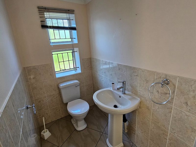A functional guest bathroom featuring a pedestal basin, toilet, and neutral wall tiling.
