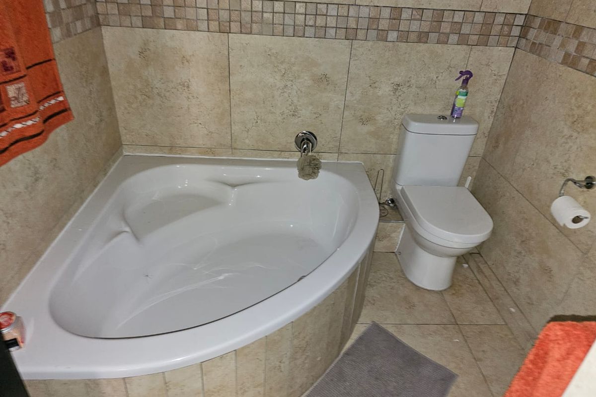 A compact bathroom featuring a corner bathtub, tiled walls with decorative mosaic accents, and a standard white toilet.