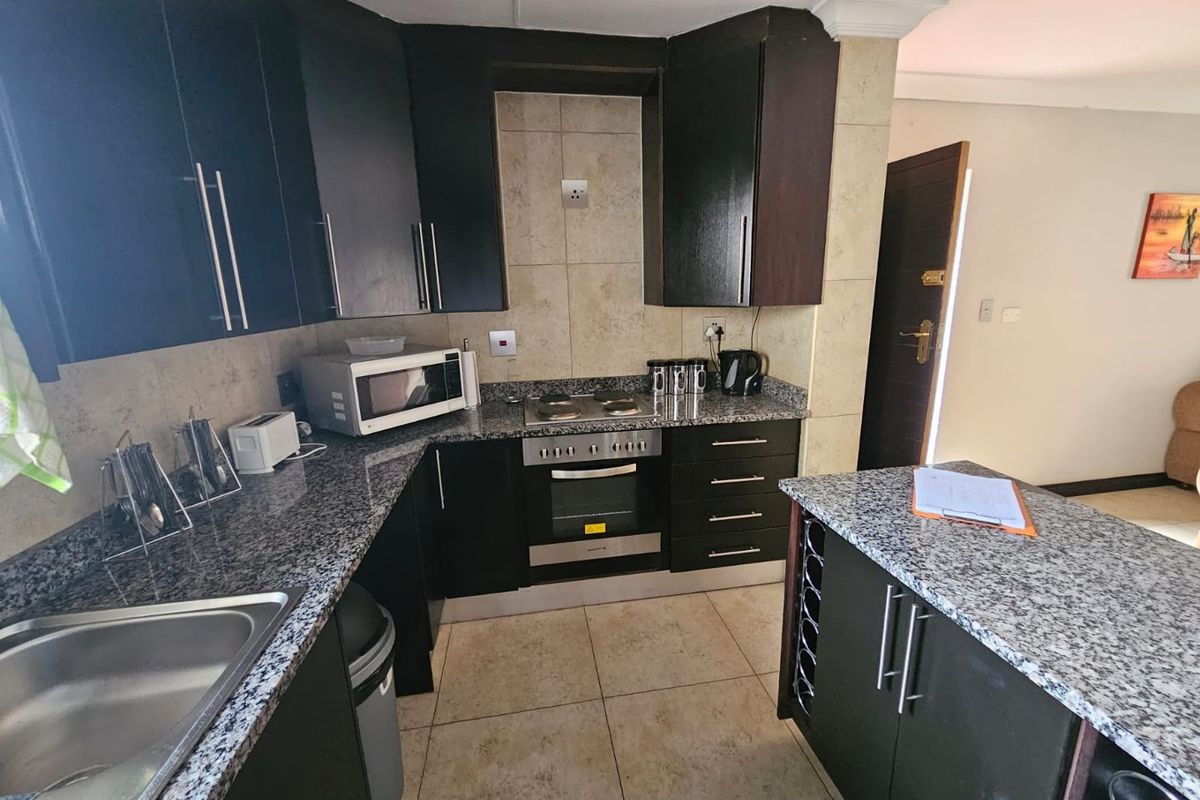 Modern kitchen featuring dark cabinetry, granite countertops, built-in oven, hob, and a functional breakfast island with integrated wine rack.