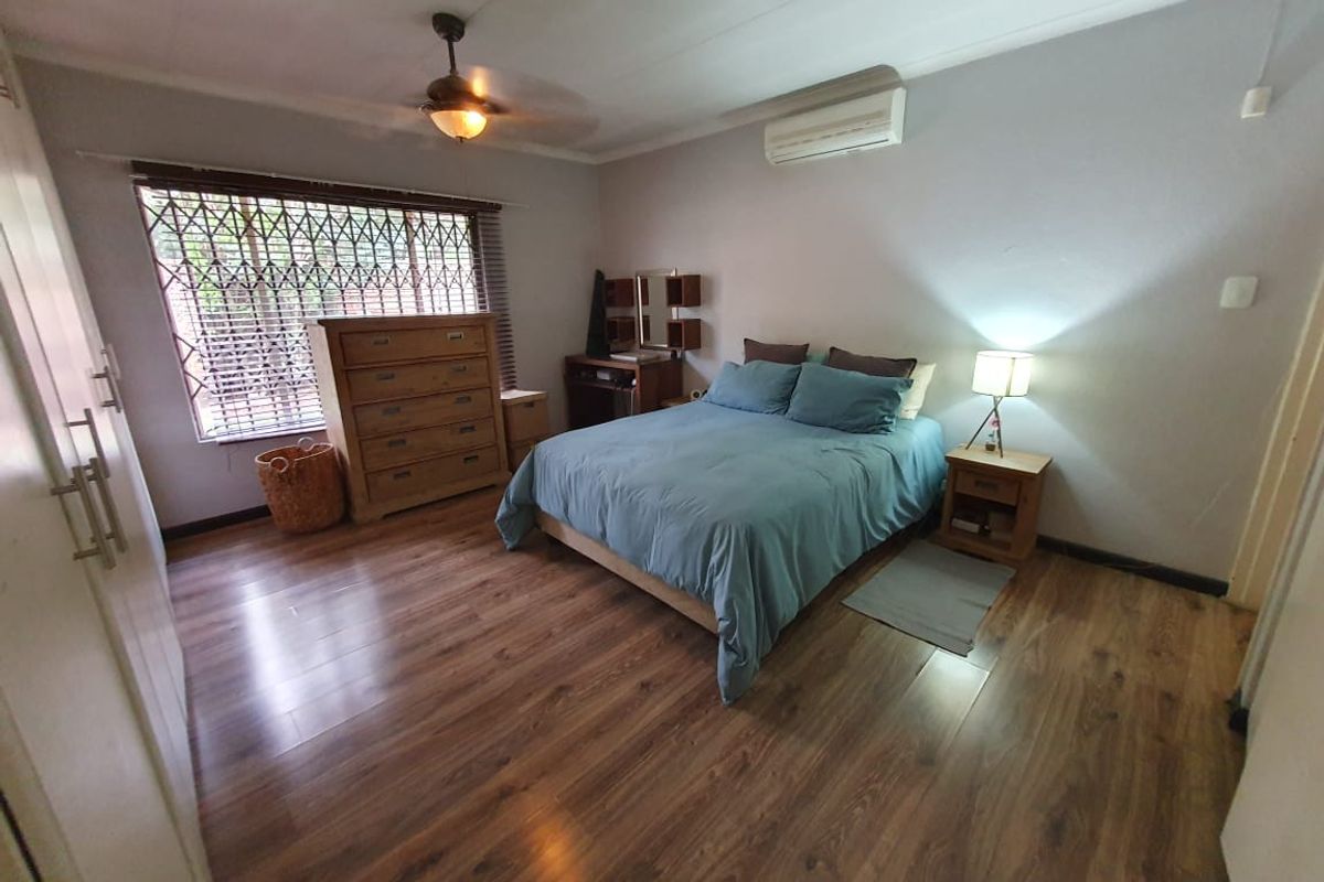 A bedroom featuring wood-look laminate flooring, a ceiling fan, and a wall-mounted air conditioning unit.
