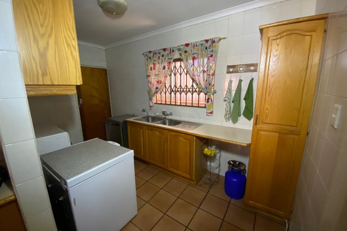A functional kitchen featuring wooden cabinetry, a double basin sink, tiled walls, and tiled flooring, providing a practical workspace.