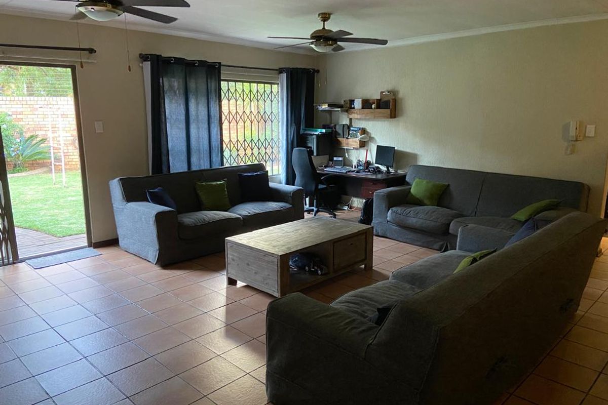 Spacious living room featuring ceramic floor tiles, dual ceiling fans, and direct access to the rear garden through a sliding glass door.