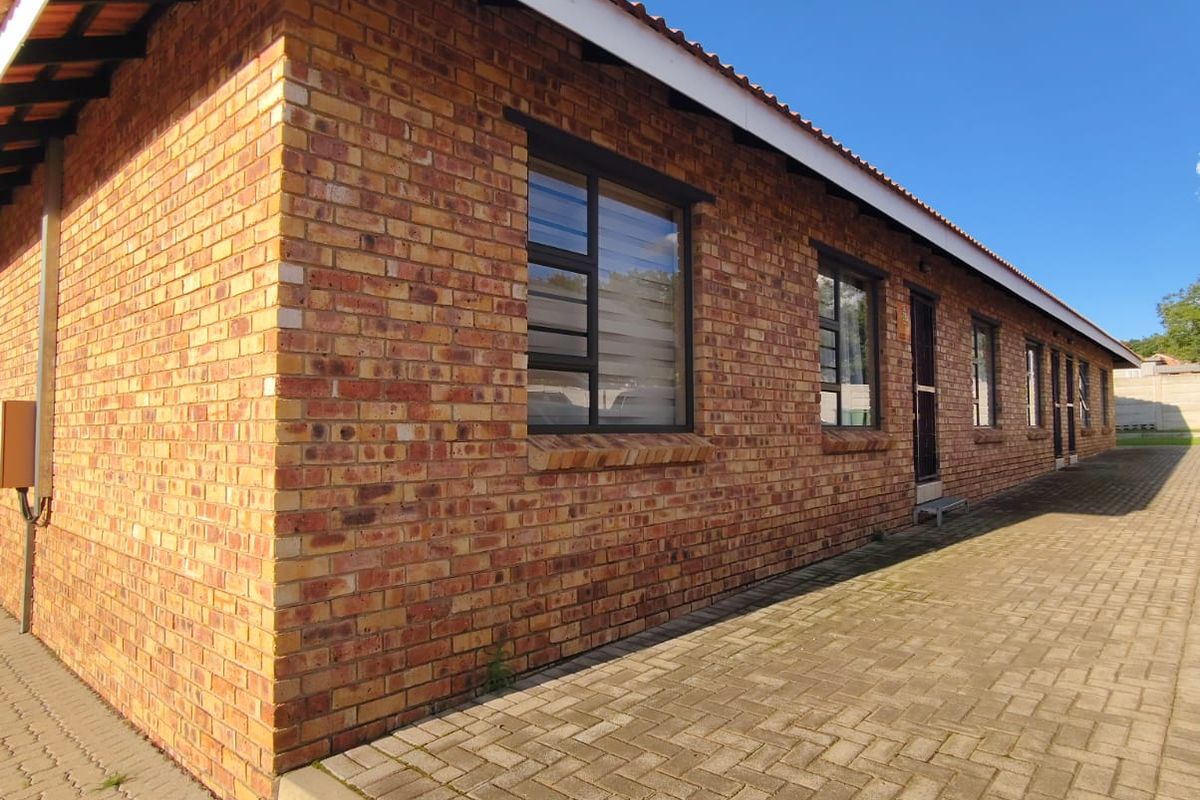 A side view of the townhouse featuring a durable face brick exterior, tiled roof, and paved walkway along the building perimeter.