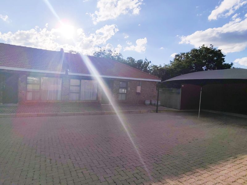 Front exterior view of the townhouse featuring a brick paved driveway and a covered carport area under a tiled roof.