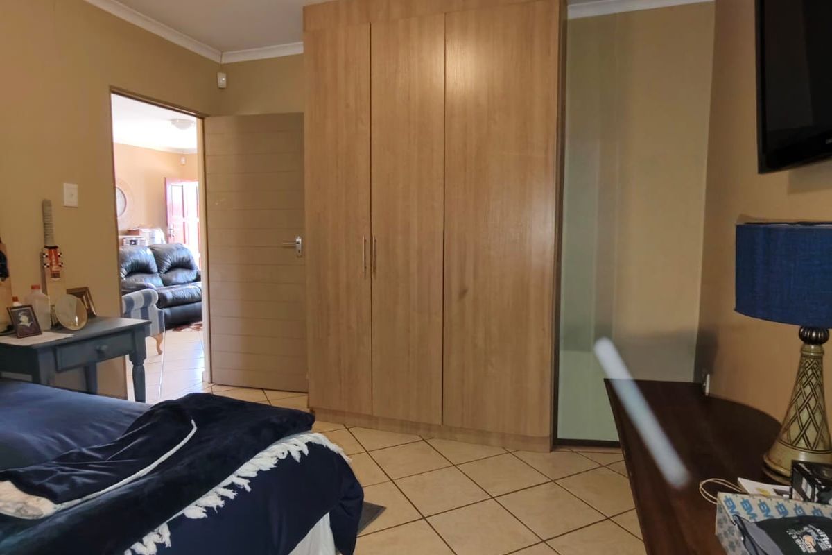 A bedroom featuring tiled flooring, a built-in wooden wardrobe, and a ceiling light fixture, with an adjacent room visible through the doorway.