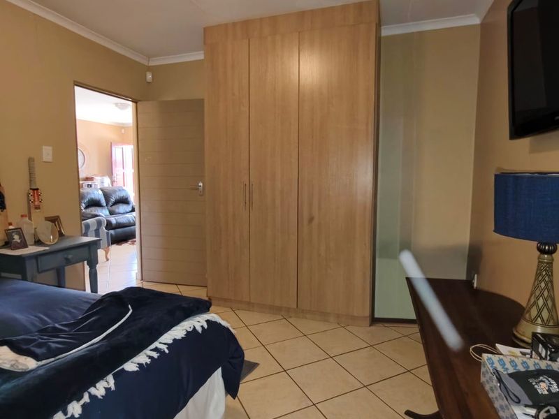 A bedroom featuring tiled flooring, a built-in wooden wardrobe, and a ceiling light fixture, with an adjacent room visible through the doorway.