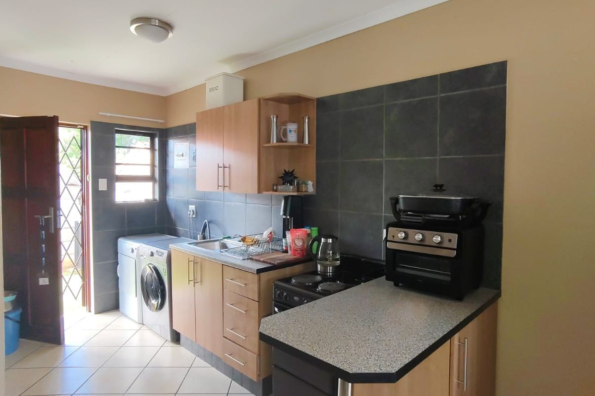 Functional kitchen featuring light wood cabinetry, dark tiled backsplash, laminate countertops, and dedicated plumbing for a washing machine.
