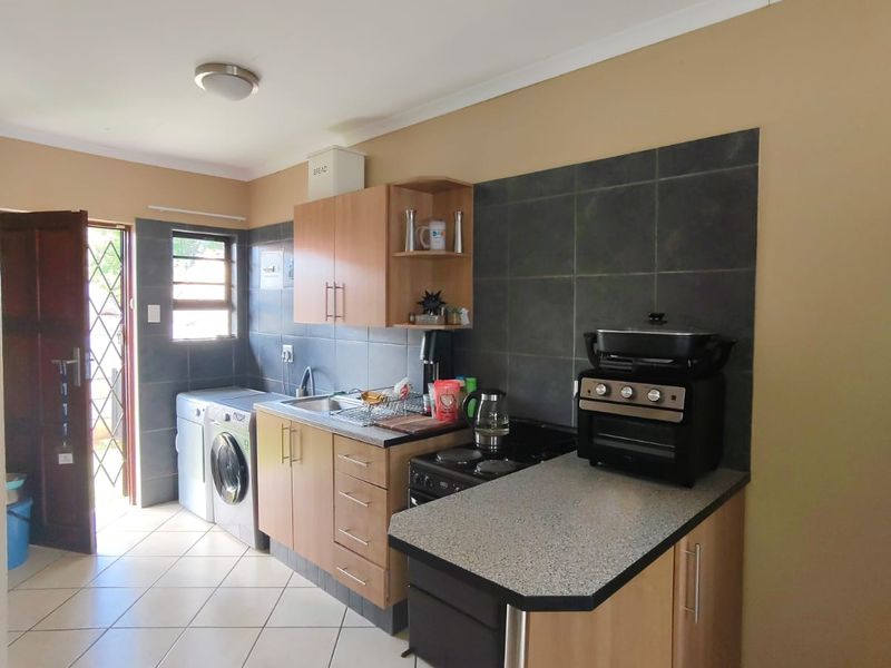 Functional kitchen featuring light wood cabinetry, dark tiled backsplash, laminate countertops, and dedicated plumbing for a washing machine.