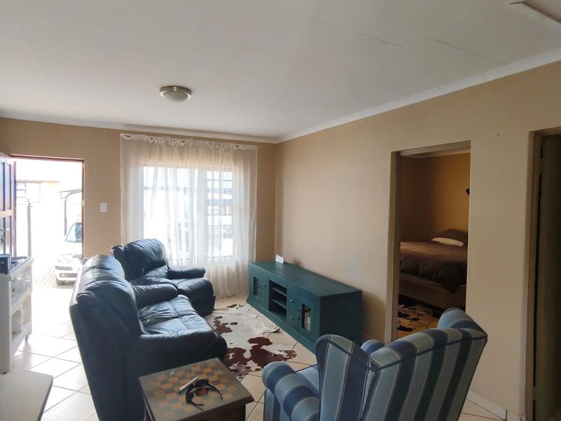 A living room area featuring tiled flooring and neutral wall tones, with direct access to an adjacent bedroom and exterior entrance.