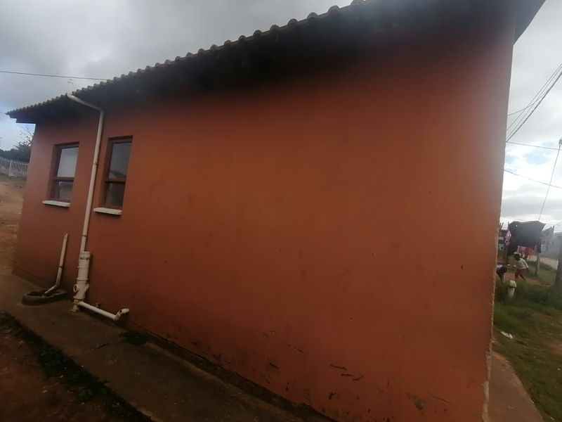 A view of the rear exterior wall of the house, featuring a tiled roof, casement windows, and exposed plumbing infrastructure.