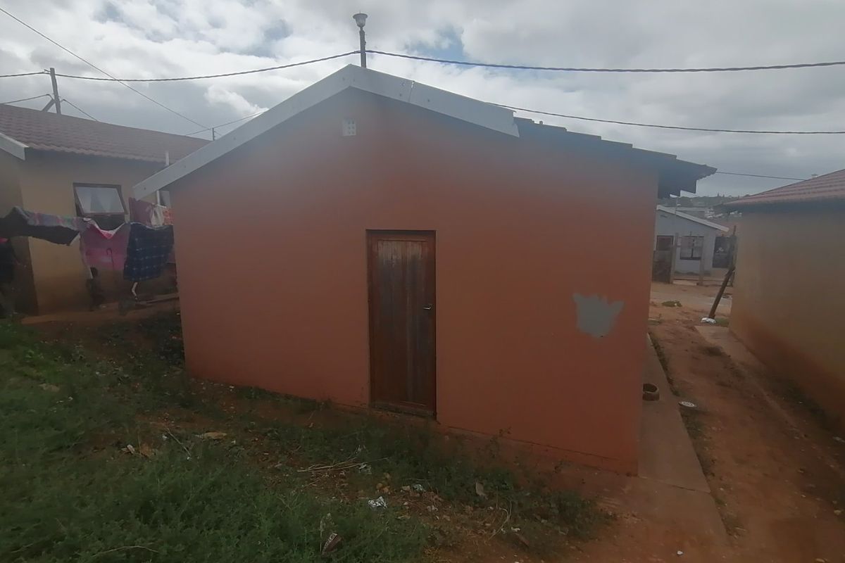 Rear view of a modest residential house featuring a simple gable roof design and a timber entrance door.