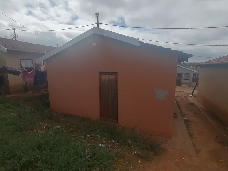 Rear view of a modest residential house featuring a simple gable roof design and a timber entrance door.