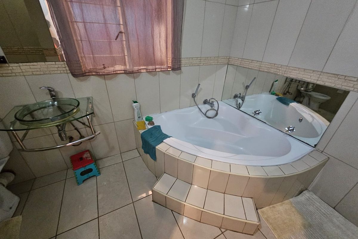 A bathroom featuring a corner jetted bathtub with tiled steps, a glass vessel sink, and wall-to-wall tiling.