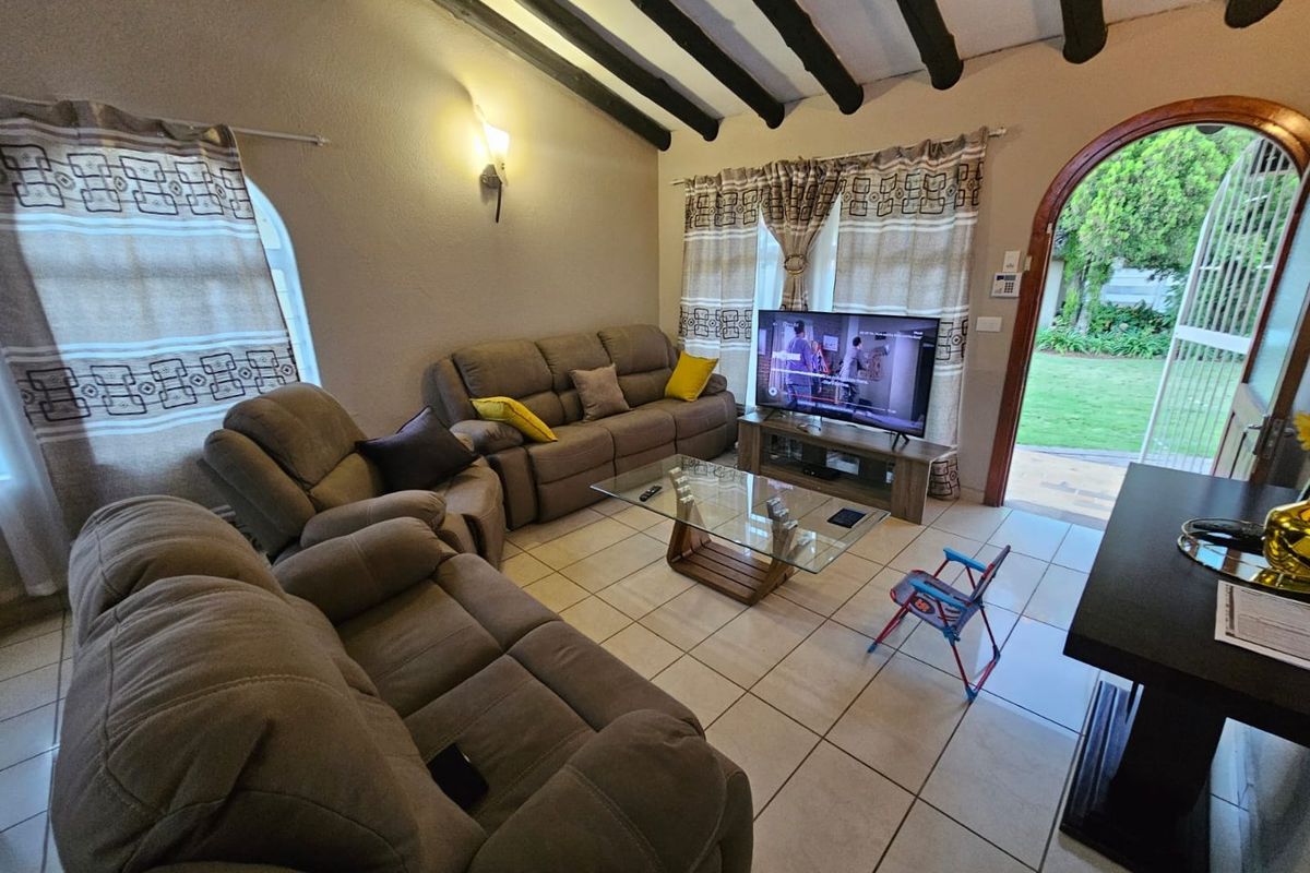 A cozy living room featuring exposed timber ceiling beams, tiled flooring, and an arched doorway providing direct access to the garden.