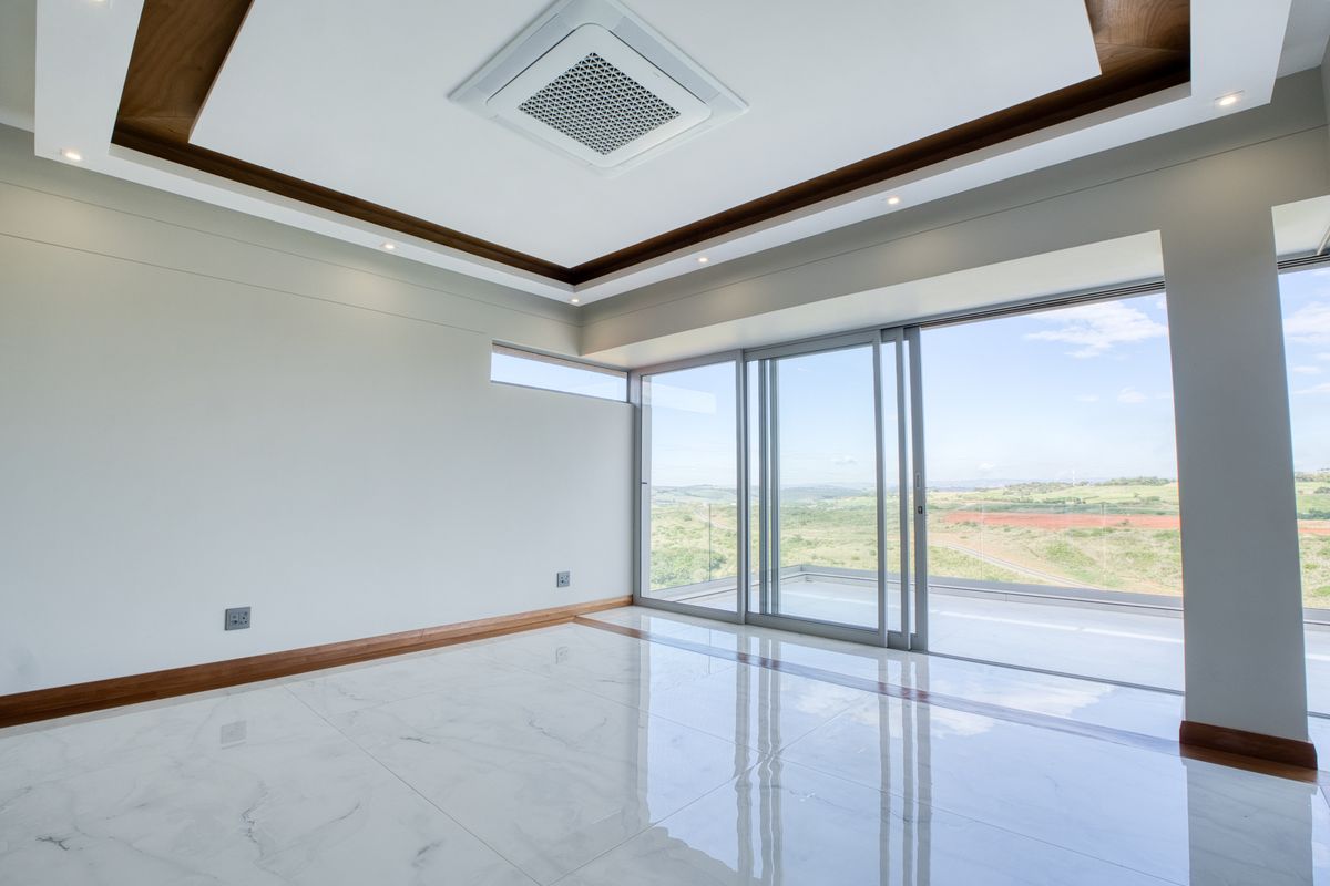 Modern living area featuring polished marble-style flooring, recessed tray ceiling with wood accents, integrated air conditioning, and large sliding glass doors opening to a balcony.