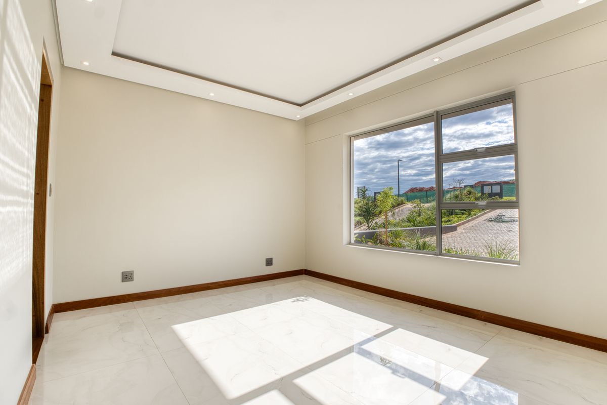 A bright, empty bedroom featuring modern recessed ceiling lighting, large windows with exterior views, and polished marble-style floor tiles.