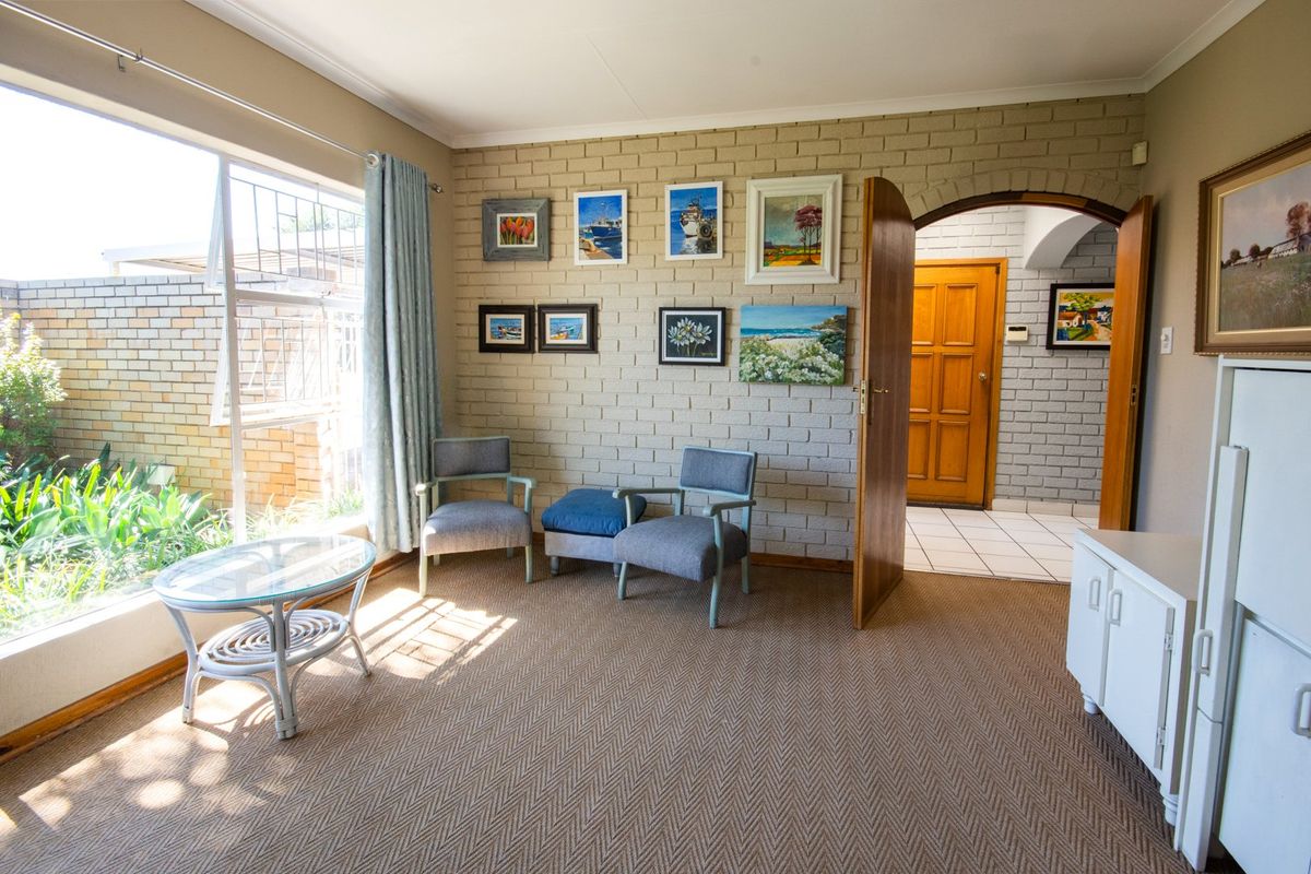 A living room featuring a large window, exposed brick wall, and arched doorway leading to an entrance hall with tiled flooring.