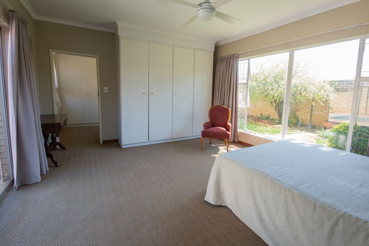 Spacious bedroom featuring built-in cupboards, carpeted flooring, and large windows providing natural light and garden views.