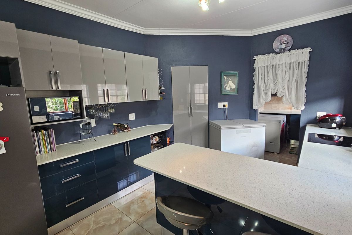 Modern kitchen featuring high-gloss cabinetry, stone-look countertops, a central island, and a dedicated scullery area with tiled flooring.