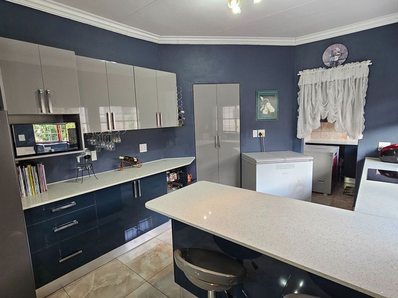 Modern kitchen featuring high-gloss cabinetry, stone-look countertops, a central island, and a dedicated scullery area with tiled flooring.
