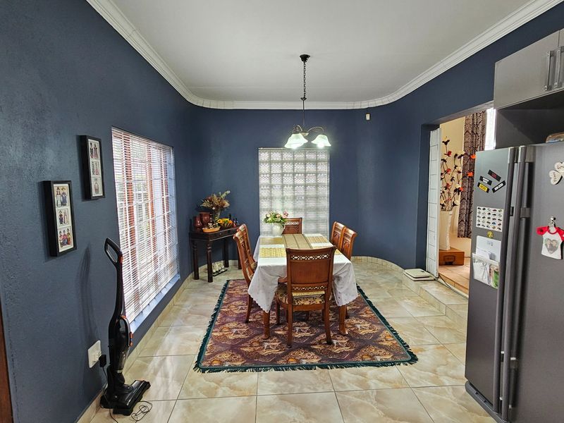 A dining area featuring tiled flooring, dark blue walls, crown molding, and a pendant light fixture, adjacent to the kitchen space.