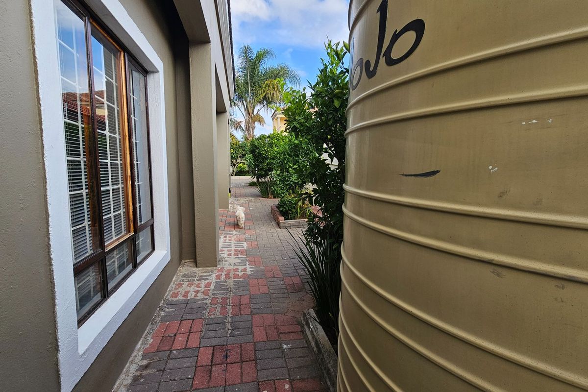 Side exterior walkway featuring paved path, exterior wall with window, and a large water storage tank.