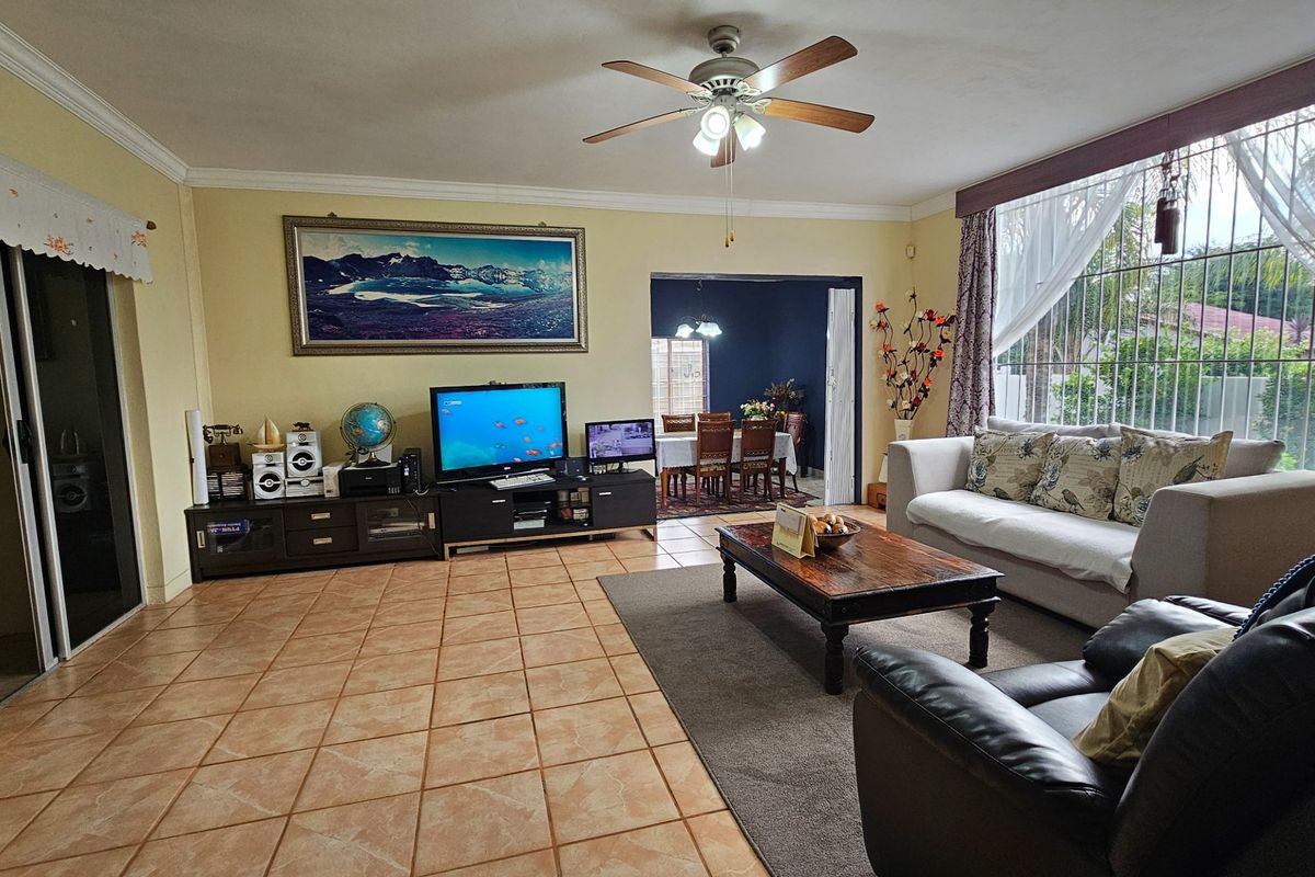 Spacious living room featuring tiled flooring, a ceiling fan, and large windows, with an open-plan flow leading into the adjacent dining area.