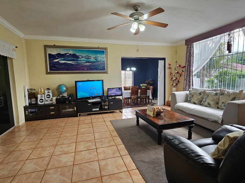 Spacious living room featuring tiled flooring, a ceiling fan, and large windows, with an open-plan flow leading into the adjacent dining area.
