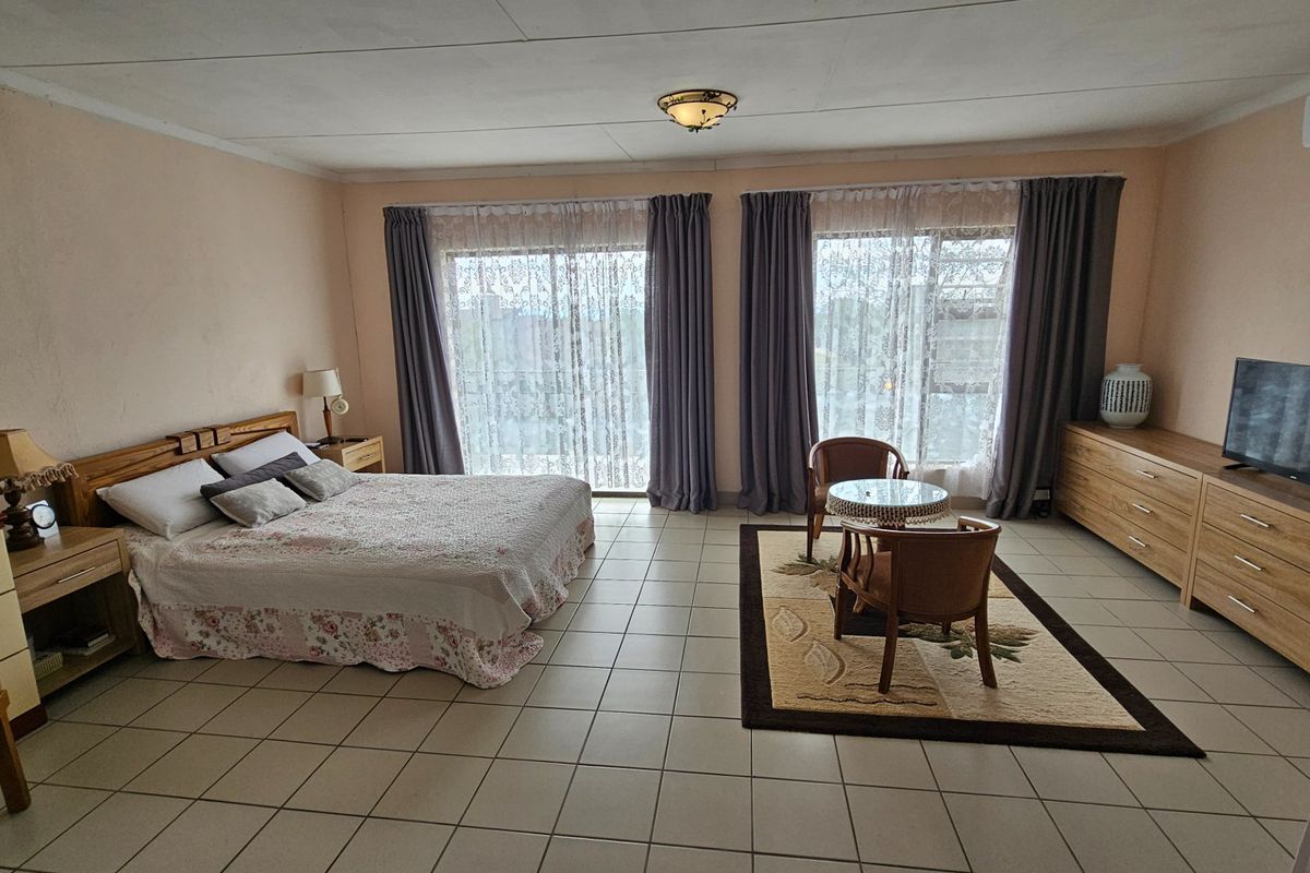 Spacious bedroom featuring tiled flooring, large sliding glass doors with curtains, and a wall-mounted air conditioning unit.
