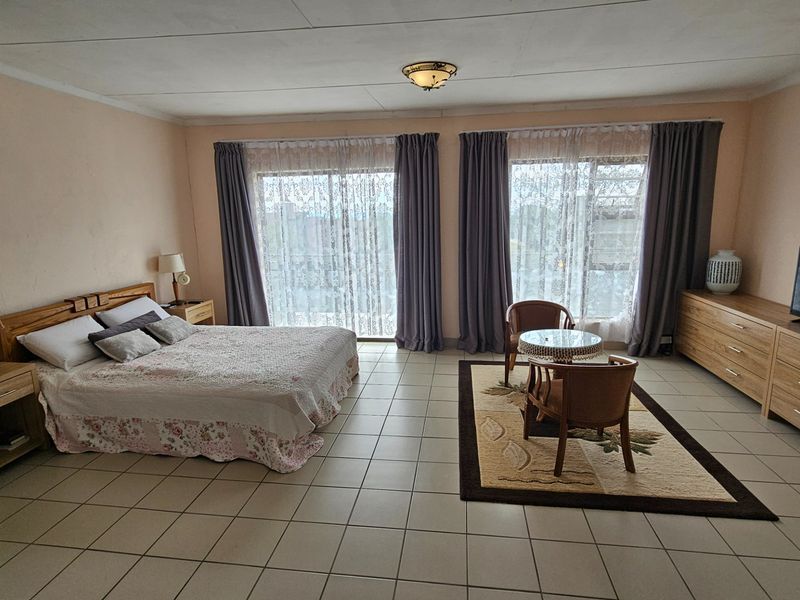 Spacious bedroom featuring tiled flooring, large sliding glass doors with curtains, and a wall-mounted air conditioning unit.