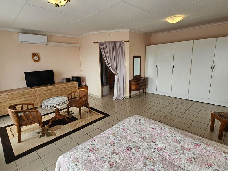 Spacious bedroom featuring built-in cupboards, tiled flooring, and a wall-mounted air conditioning unit.