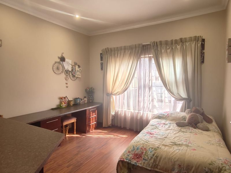 A well-lit bedroom featuring laminate flooring, recessed downlights, and a functional built-in desk area with integrated storage drawers.