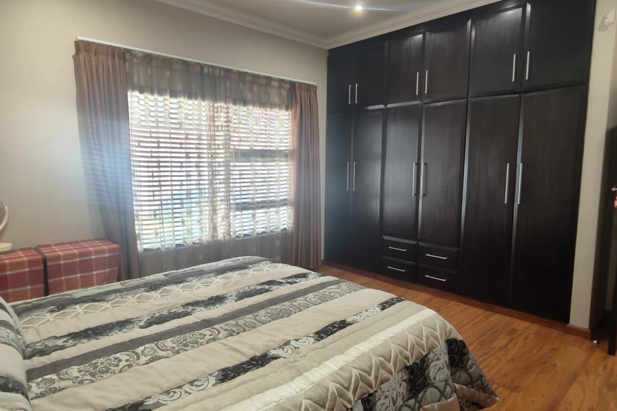 A well-maintained bedroom featuring dark wood built-in cupboards, warm laminate flooring, and recessed ceiling lighting.