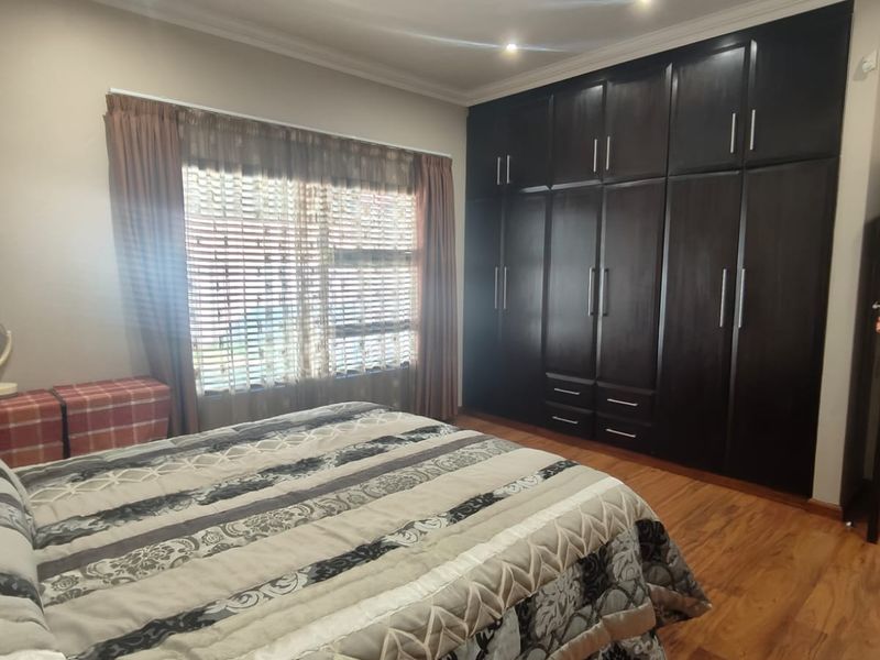 A well-maintained bedroom featuring dark wood built-in cupboards, warm laminate flooring, and recessed ceiling lighting.