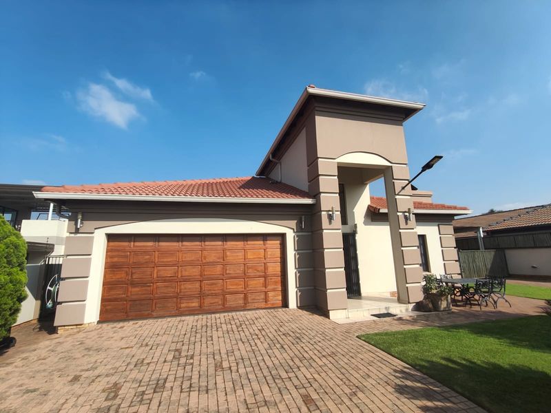 Front elevation of a well-maintained house featuring a paved driveway, a prominent wooden garage door, and a covered entrance with architectural detailing.