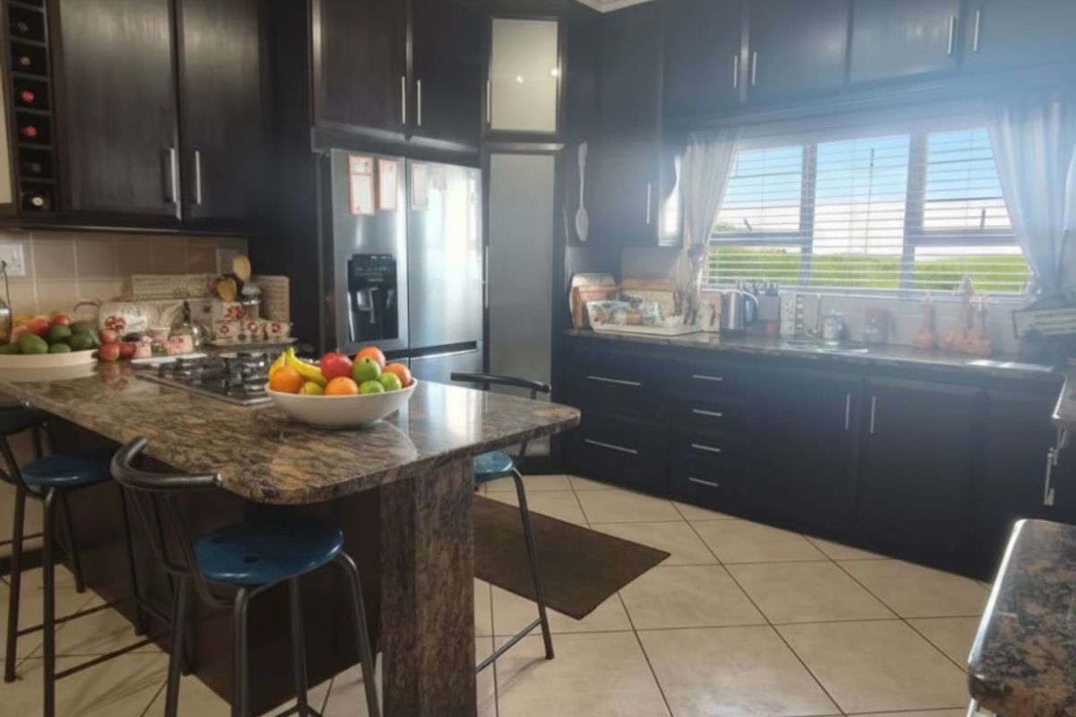 A well-appointed kitchen featuring dark wood cabinetry, granite countertops, a central island with breakfast bar seating, and ceramic tiled flooring.