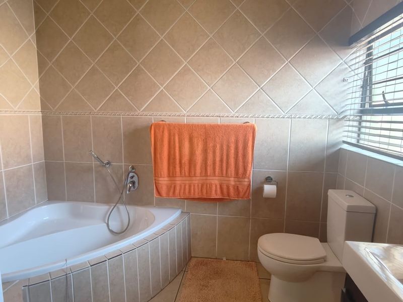 A functional bathroom featuring a corner bathtub with handheld shower mixer, tiled walls, and tiled flooring.