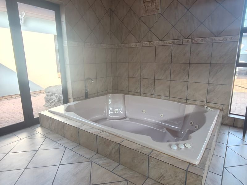 A spacious bathroom featuring a large built-in spa bath, neutral tiled finishes, and direct access to an outdoor area through sliding glass doors.
