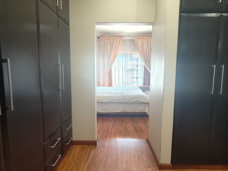A bedroom dressing area featuring extensive dark wood built-in cupboards and warm-toned laminate flooring, leading into the main sleeping area.