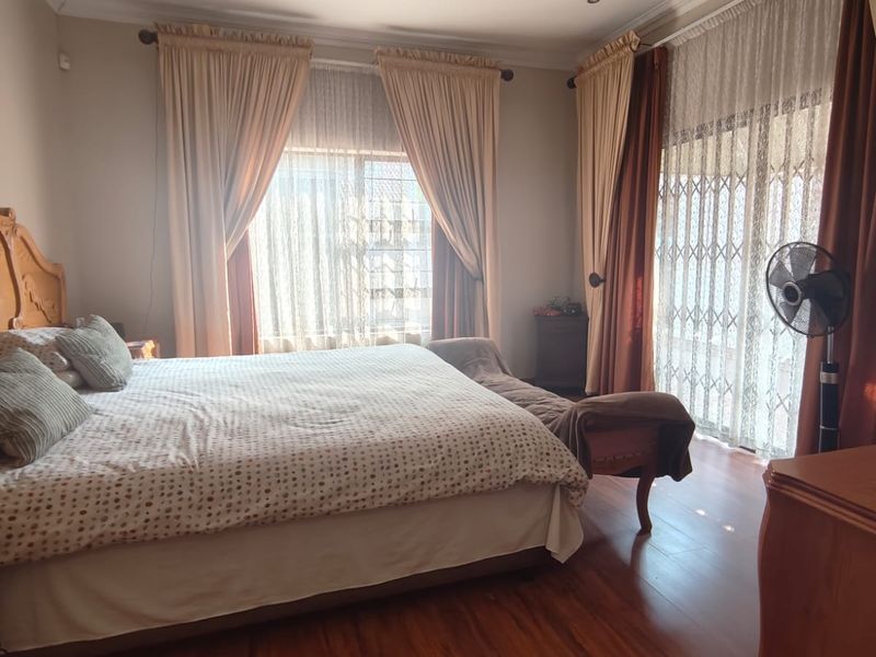 A spacious bedroom featuring warm-toned laminate flooring, recessed lighting, and large windows with access to an outdoor area through a secure sliding door.