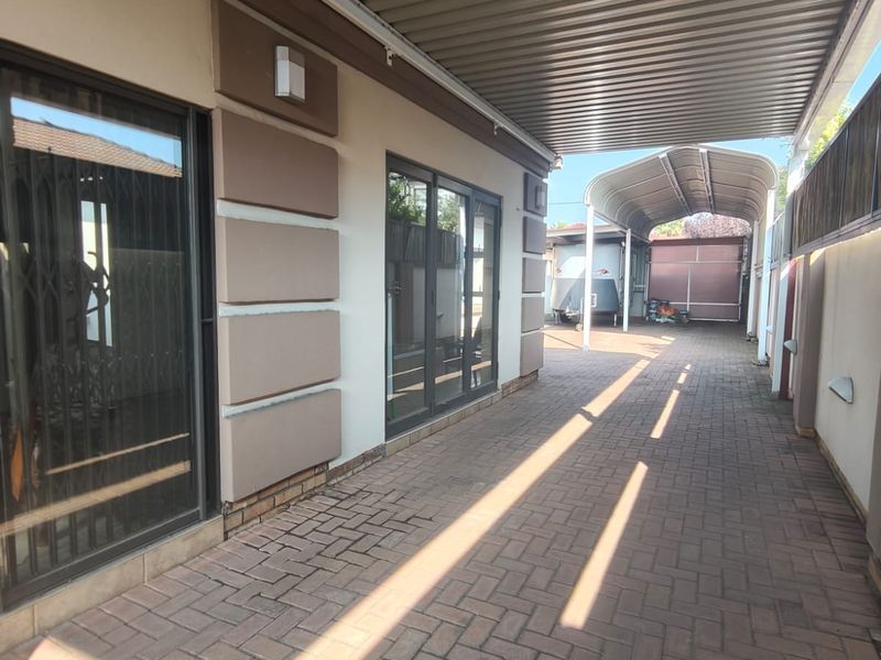 A covered paved walkway and patio area featuring corrugated metal roofing, providing access to the main dwelling and rear parking structure.