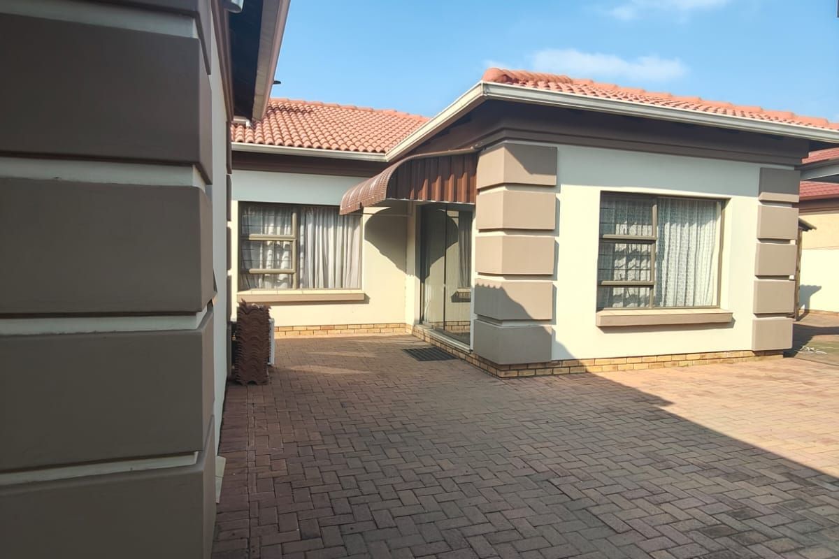 A well-maintained rear exterior view featuring a paved courtyard, terracotta roof tiles, and secure aluminium-framed windows.