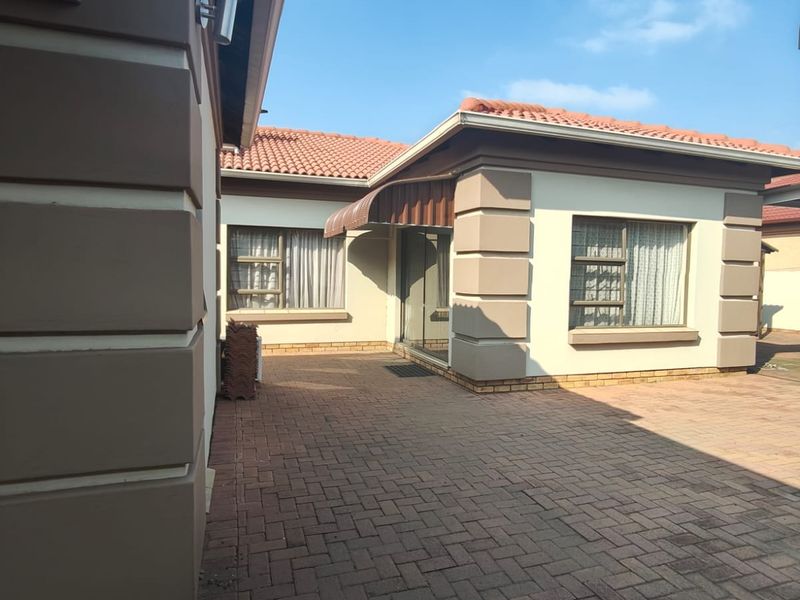 A well-maintained rear exterior view featuring a paved courtyard, terracotta roof tiles, and secure aluminium-framed windows.