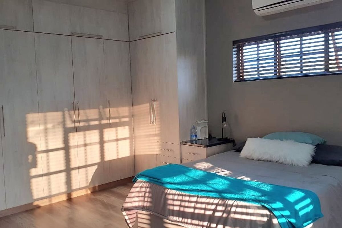 A well-lit bedroom featuring extensive built-in cabinetry, light wood-look flooring, and a wall-mounted air conditioning unit.