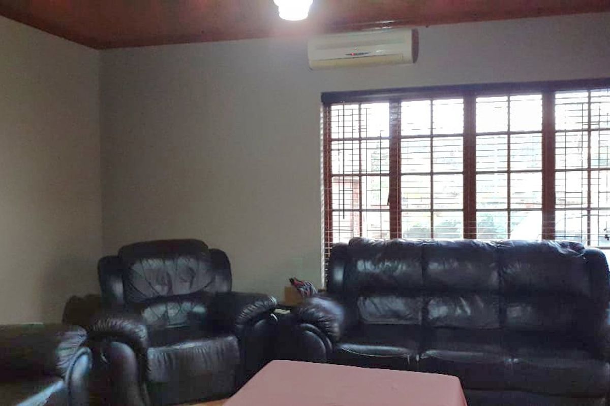 A living room featuring a wooden ceiling, large window with blinds, and a wall-mounted air conditioning unit.