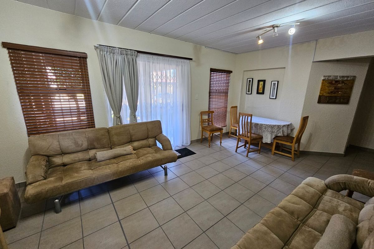 A spacious living and dining area featuring neutral tiled flooring, slatted window blinds, and a sliding glass door providing access to the exterior.